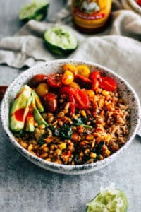 Easy tempeh burrito bowls in white ceramic bowl with lime and hot sauce in the background.