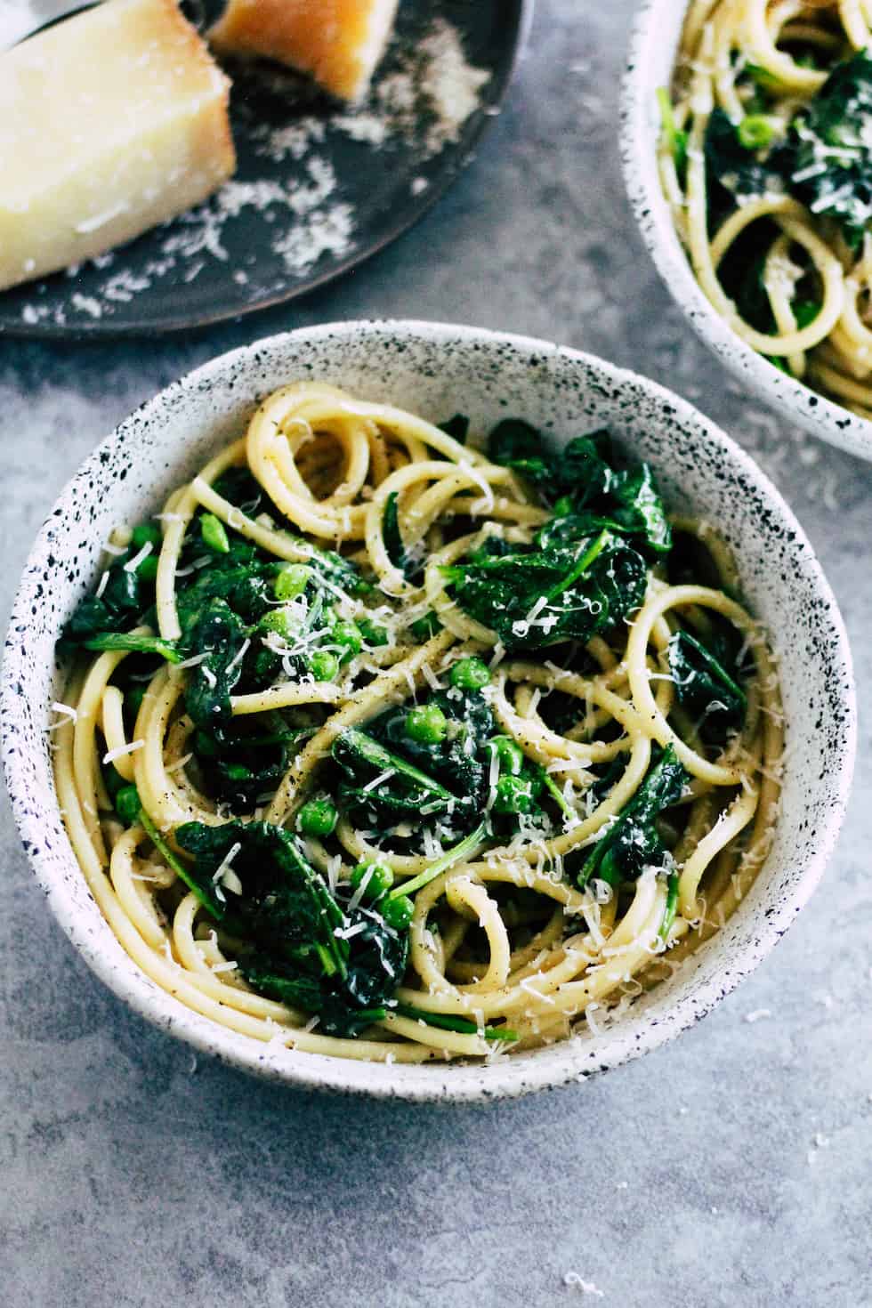 Cacio e Pepe in ceramic bowl with spinach and peas. Cheese wedges in the background.