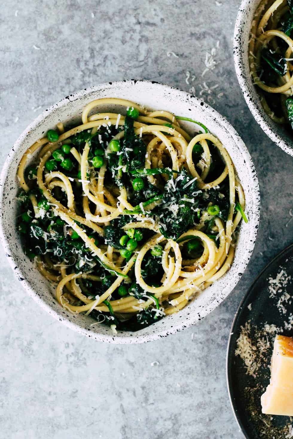 Pasta with spinach and green peas against grey background.