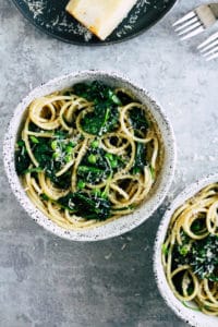 Pasta with spinach and peas in ceramic bowl with wedge of cheese.
