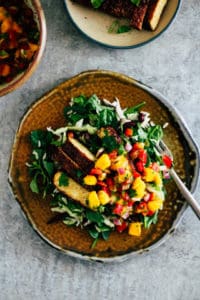 Jerk tempeh salad with mango salsa on ceramic plate with fork.