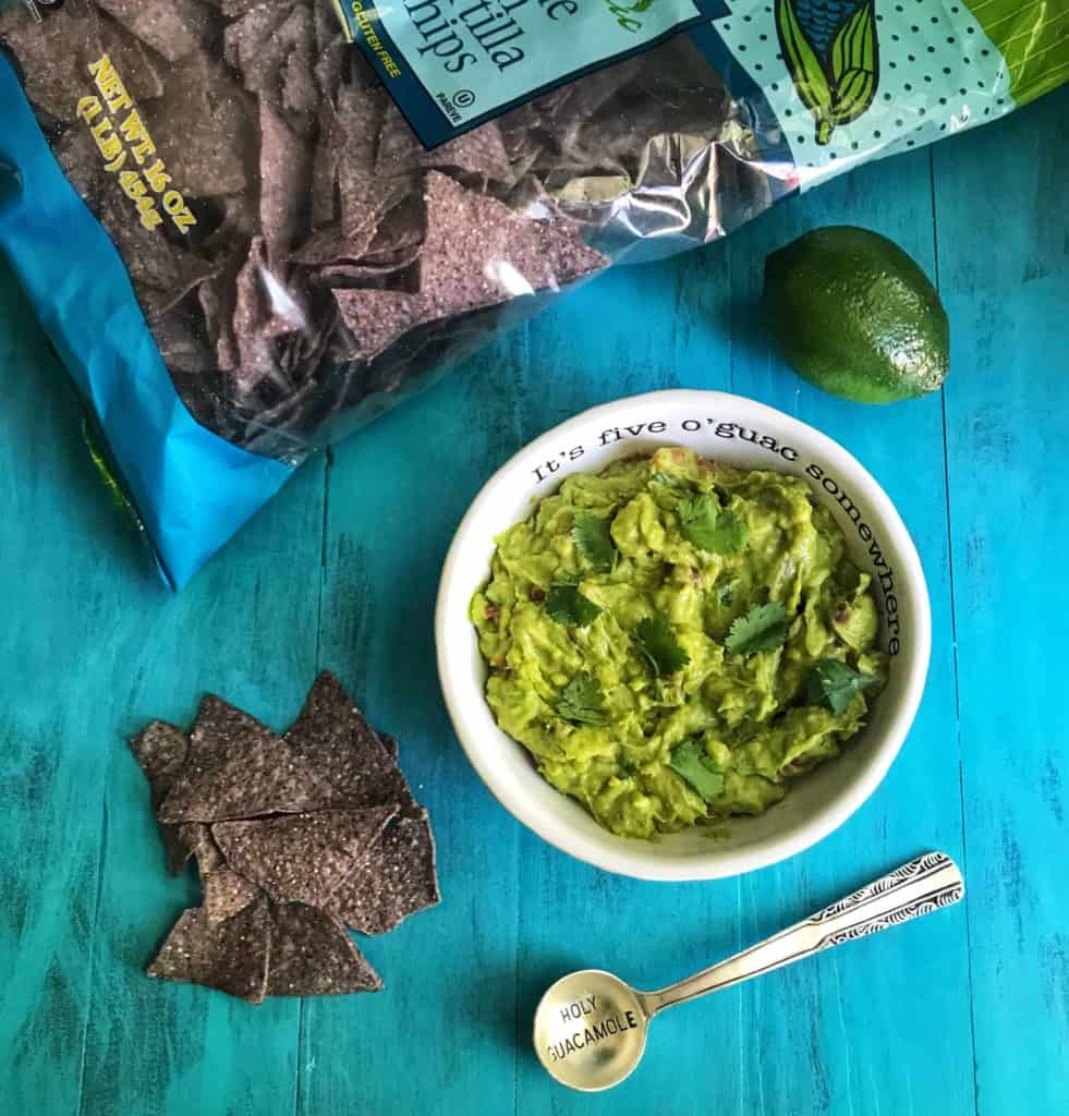 Plant-based snack ideas including guacamole in a bowl with chips against blue background.