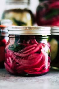 Mason jar of red onion quick pickles on grey countertop.