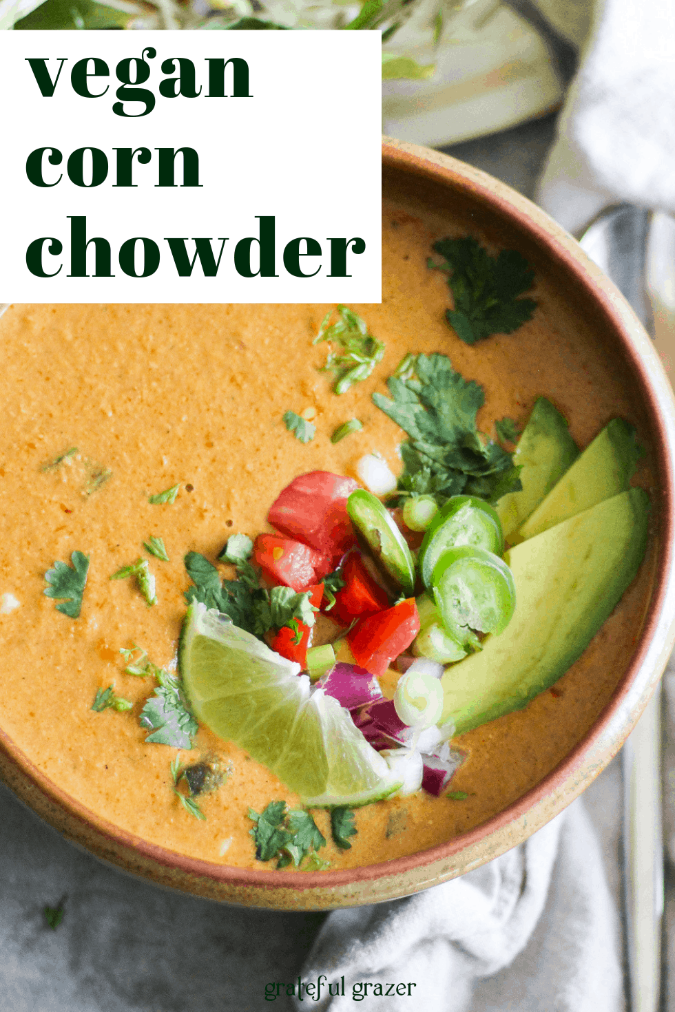 Vegan corn chowder soup with lime and avocado in a brown bowl with text that reads "vegan corn chowder."