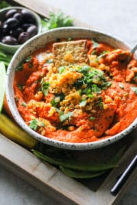 Creamy Roasted Red Pepper Lentil Dip in a white ceramic bowl on wood serving tray.