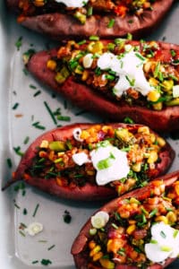 Loaded sweet potatoes in grey baking dish with chives and yogurt.