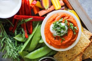 Red Lentil Hummus in white bowl on snack board with vegetables.