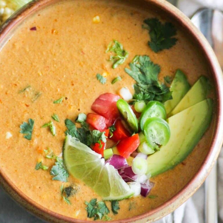 Creamy vegan corn chowder made with oat milk and topped with avocado, tomato, and lime.