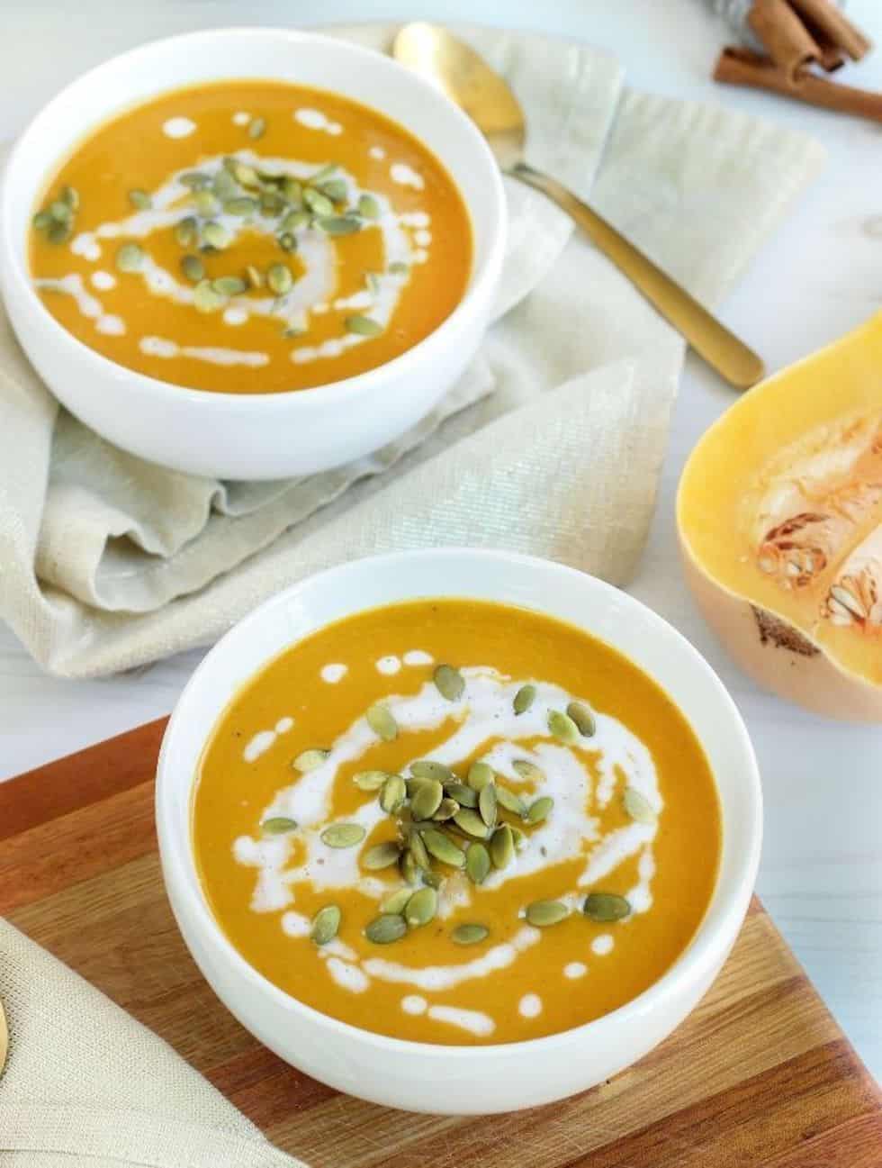 Squash soup in white bowls with sour cream swirl.