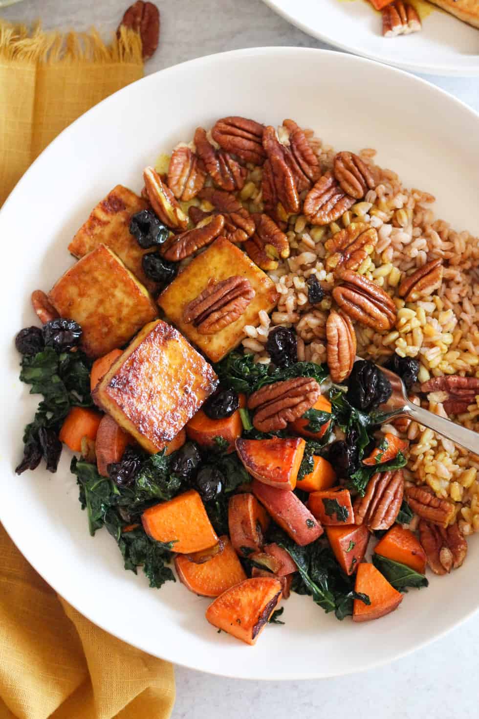 Baked tofu bowls with sweet potatoes and kale in white bowl with yellow napkin.