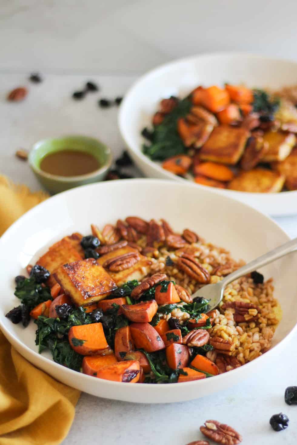 Baked Tofu Harvest Bowls with sweet potato and kale in white bowls with yellow napkin.