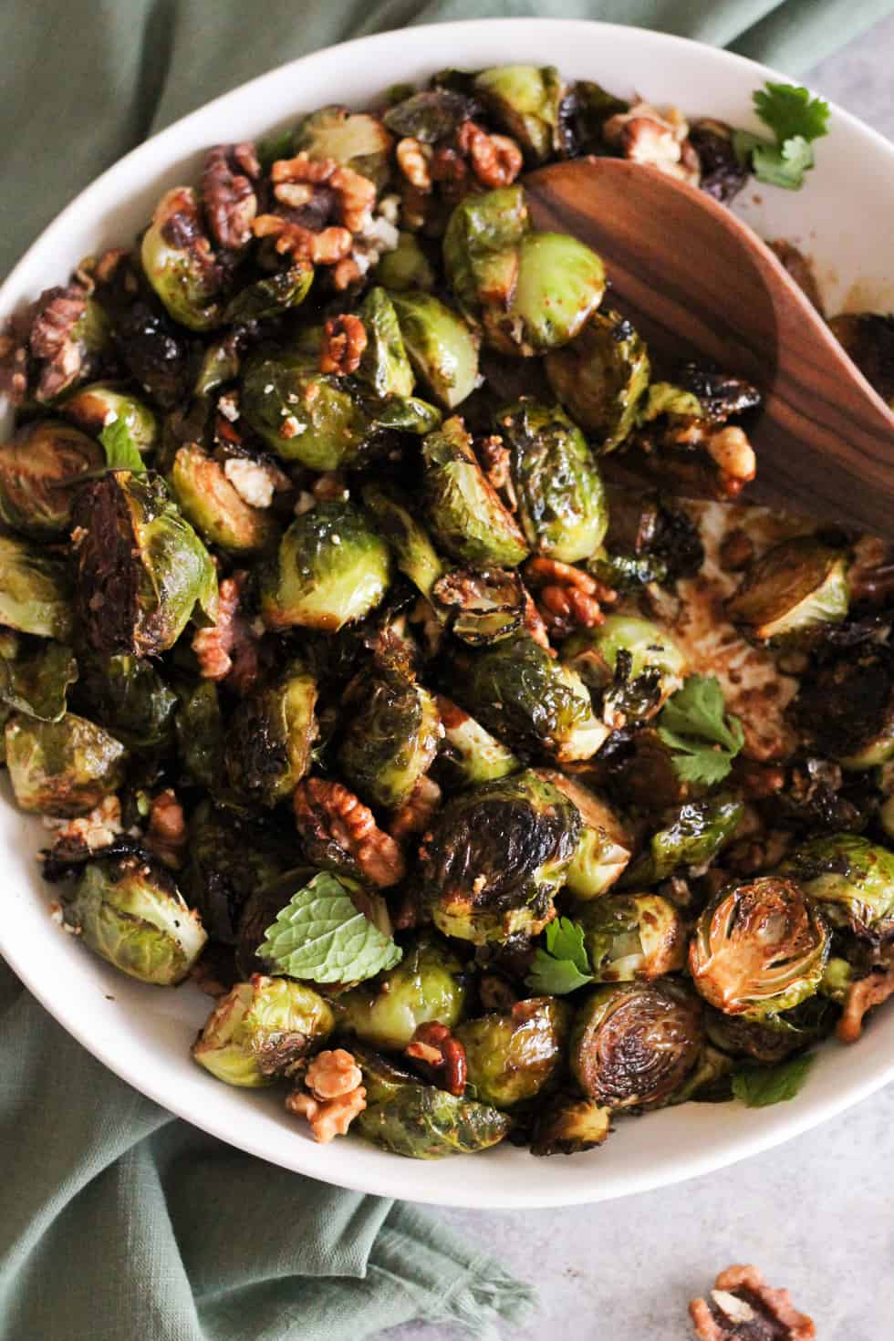 Closeup image of crispy roasted brussels sprouts in white dish with wooden spoon.