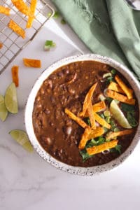 Instant Pot Black Bean Soup in white bowl with tortilla strips and green napkin.