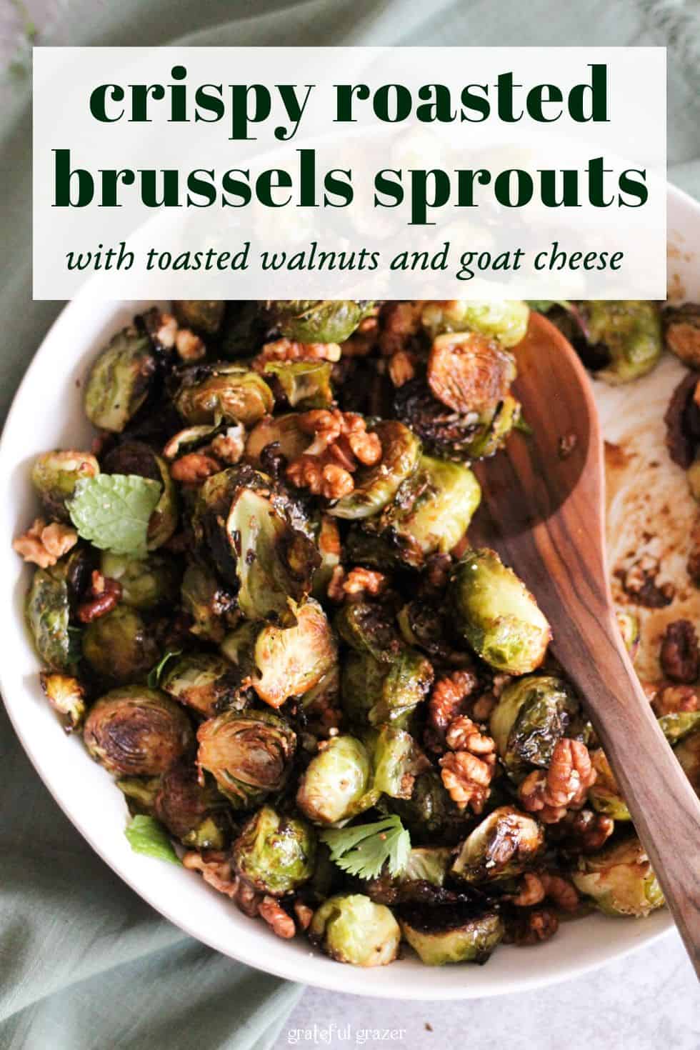 Brussels sprouts and walnuts in white dish with wooden spoon. Text reads, "Crispy Roasted Brussels Sprouts with Toasted Walnuts and Goat Cheese."