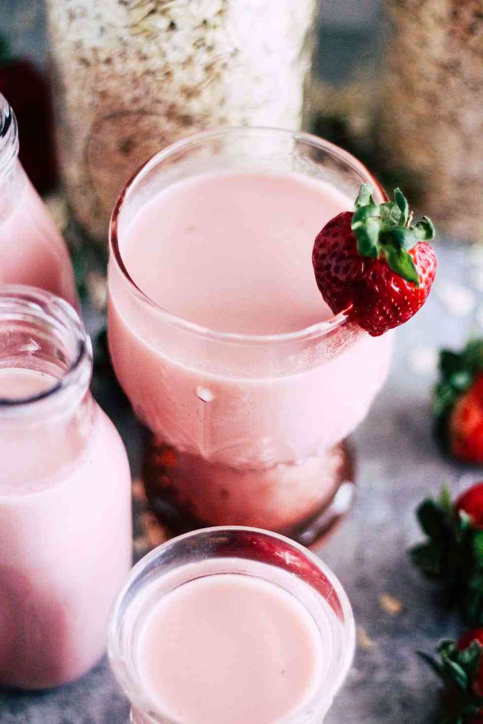 Vegan Strawberry Oat Milk in a pink glass with strawberry milk bottles next to it.