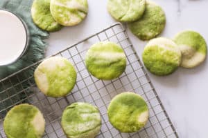 Horizontal image of marbled matcha sugar cookies on wire rack with a glass of milk.