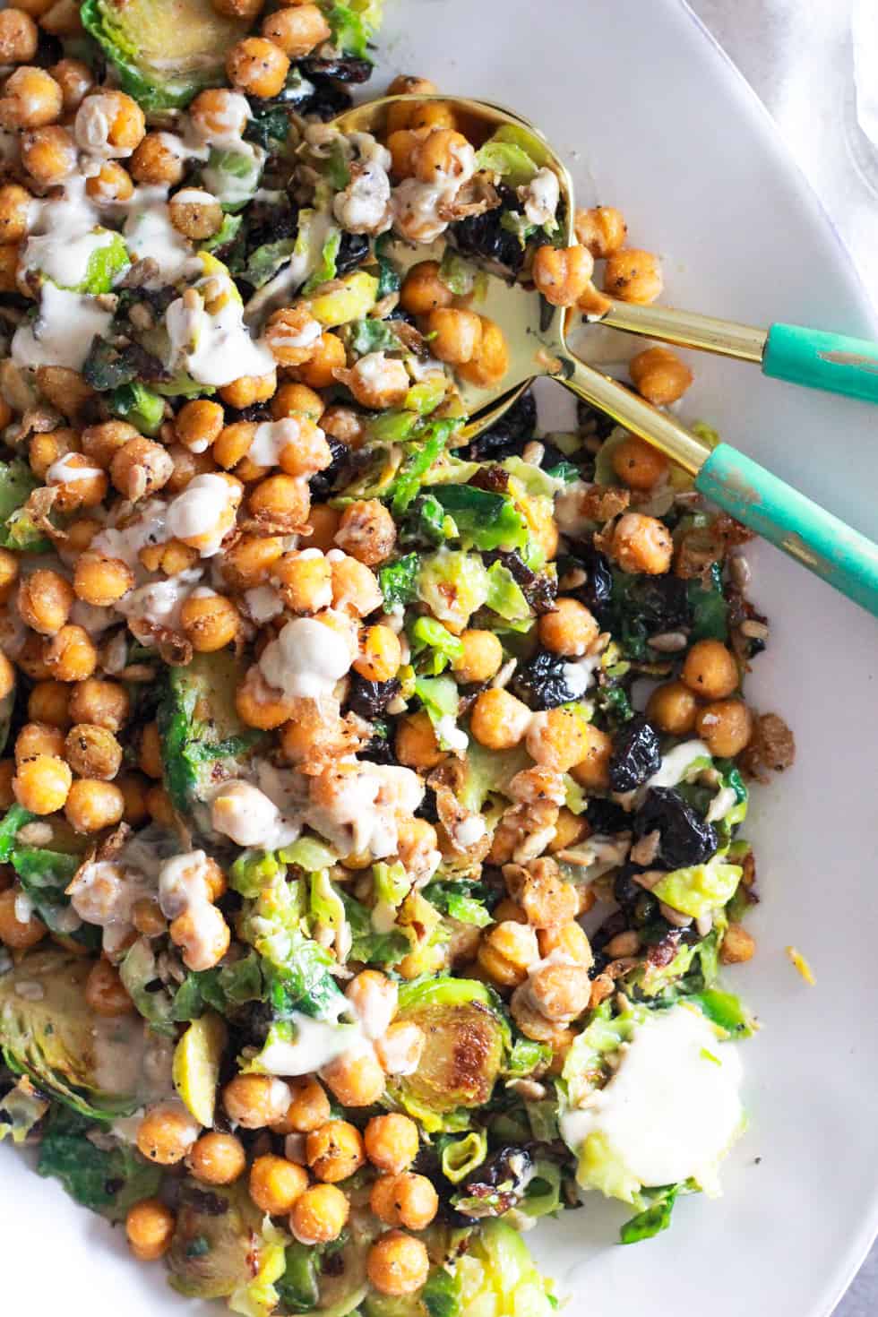 Chickpea and Brussels sprouts salad on white platter with gold utensils.