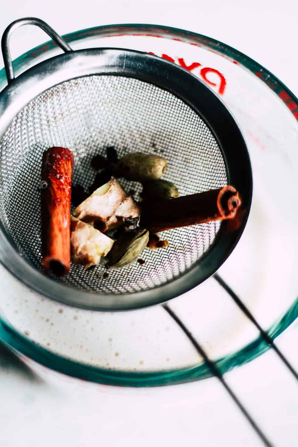 Straining whole spices from oat milk with a fine mess strainer.