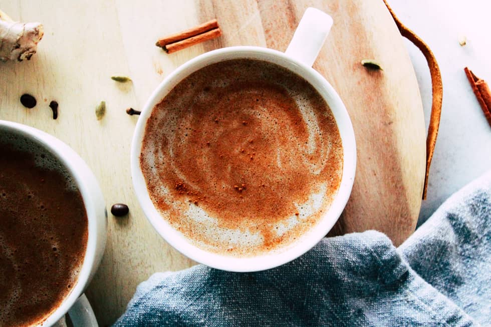 Ice coffee in glass mug with milk and cinnamon on wooden table in