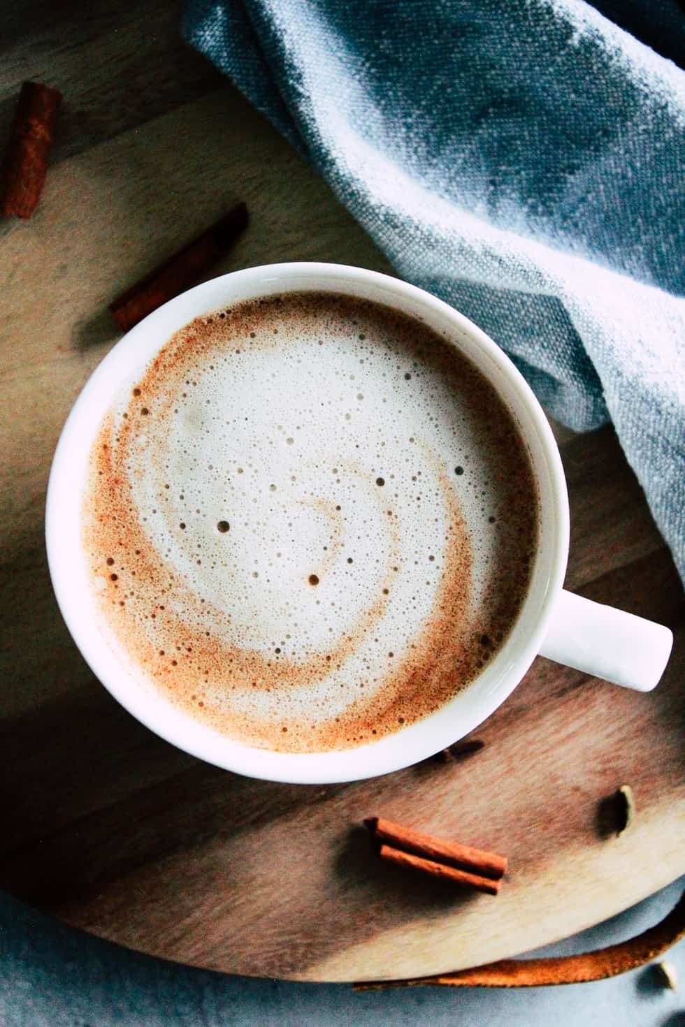 Oat Milk Latte in white mug with blue napkin and spices.