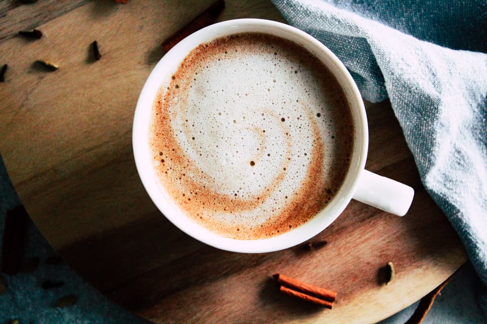 Cinnamon latte in white mug on wood tray with spices.