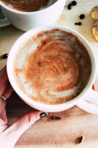 Hand holding a white mug with cinnamon latte.