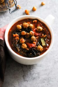 Tomato soup with roasted chickpeas in white mug.