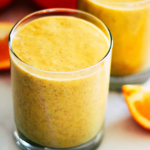Yellow Mango Orange Smoothie in a glass surrounded by oranges.