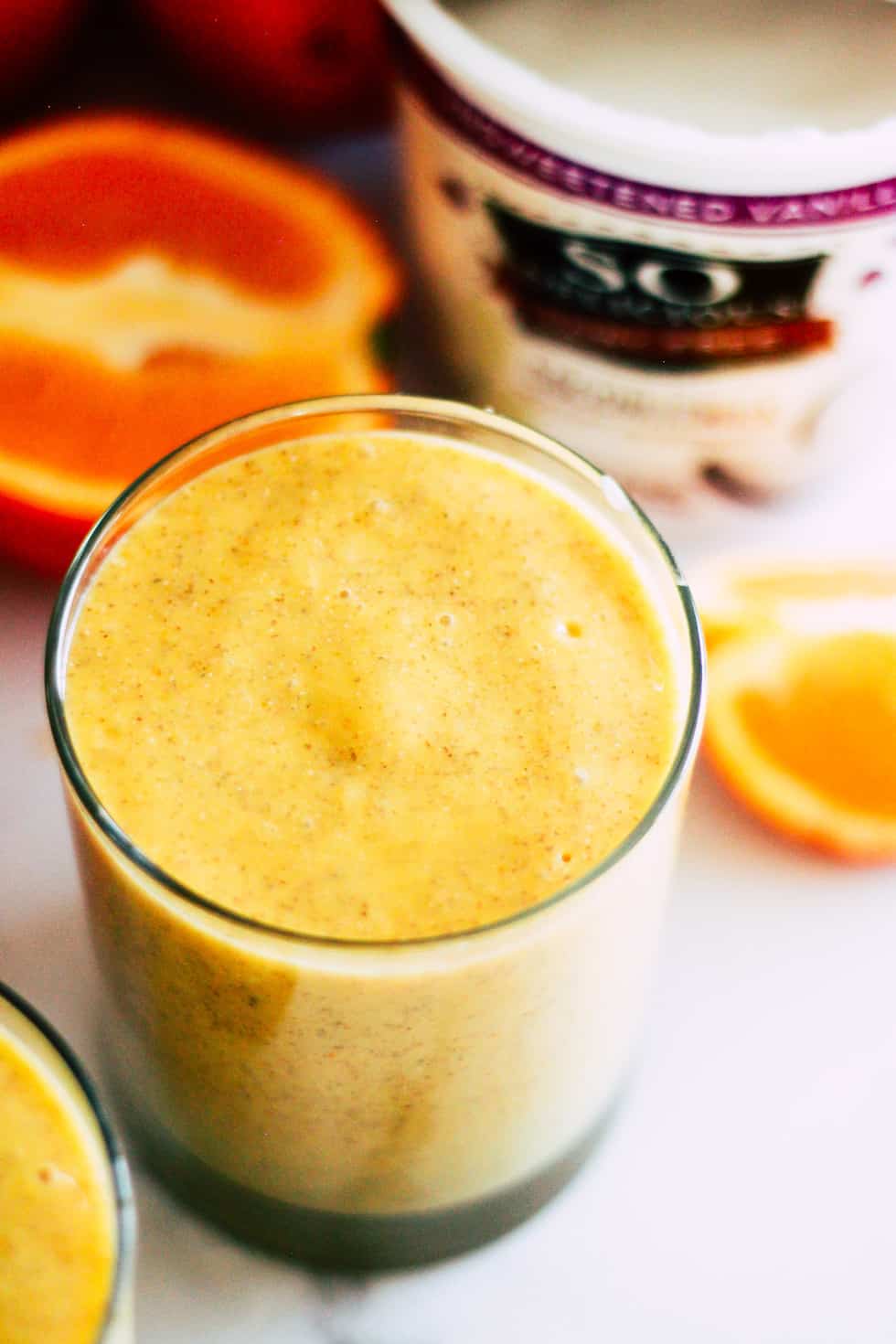 Orange Smoothie in a glass in front of oranges and a container of So Delicious yogurt.