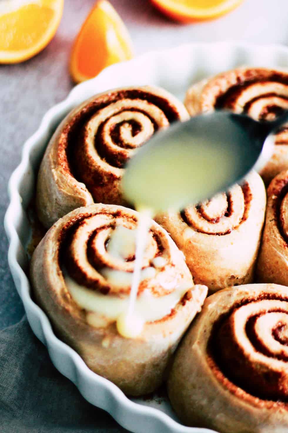 Spoon glazing icing over sweet rolls in a round, white baking dish.