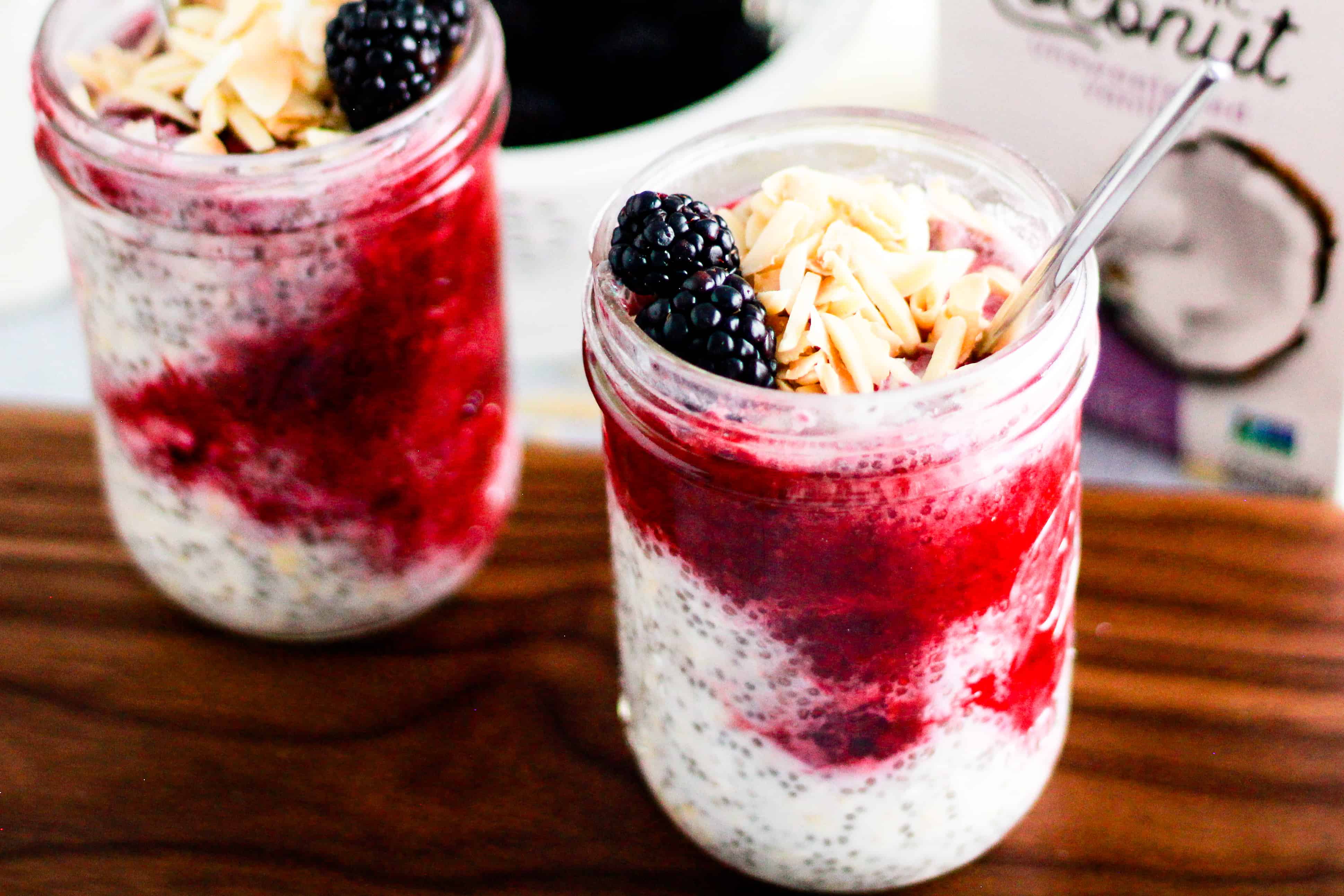 Jars of overnight oats with blackberries and carton of So Delicious Coconutmilk.