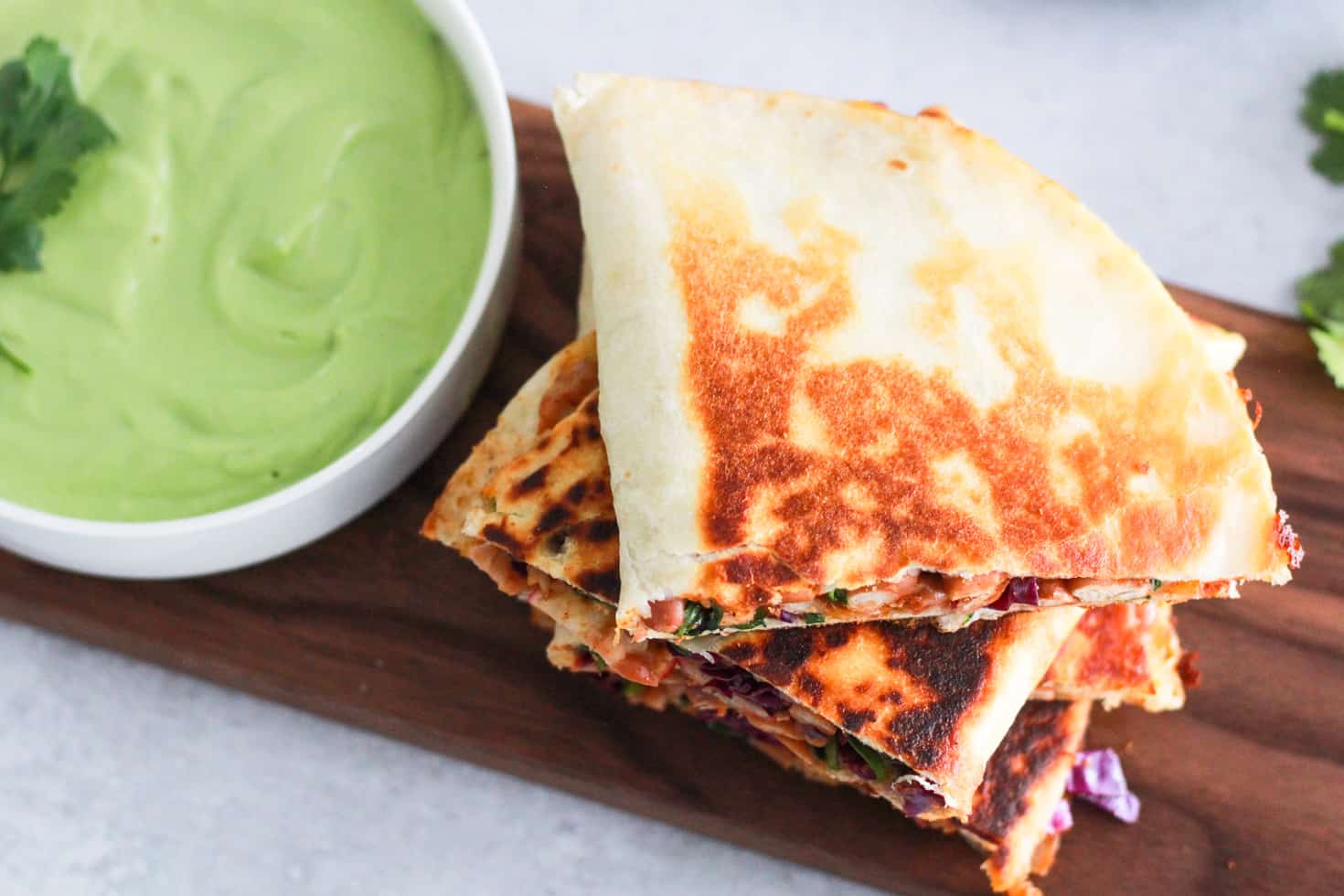 Horizontal image of bean quesadilla on wood board with avocado sauce.