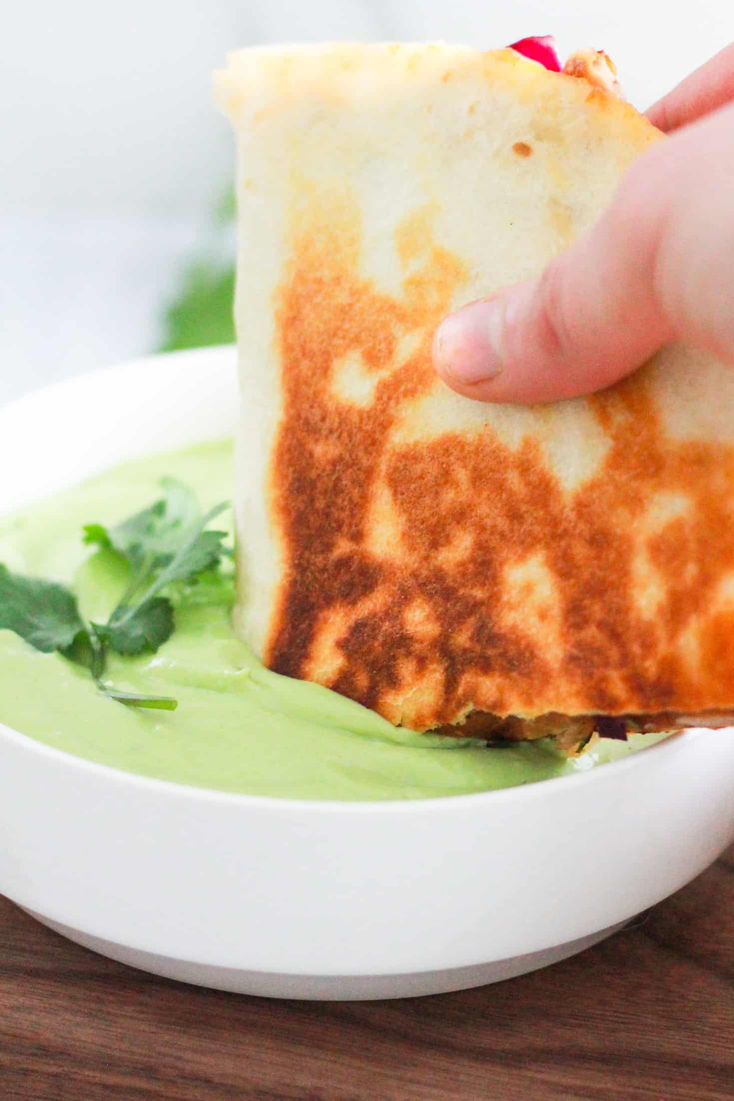 Dipping a vegetarian quesadilla into green avocado crema sauce.