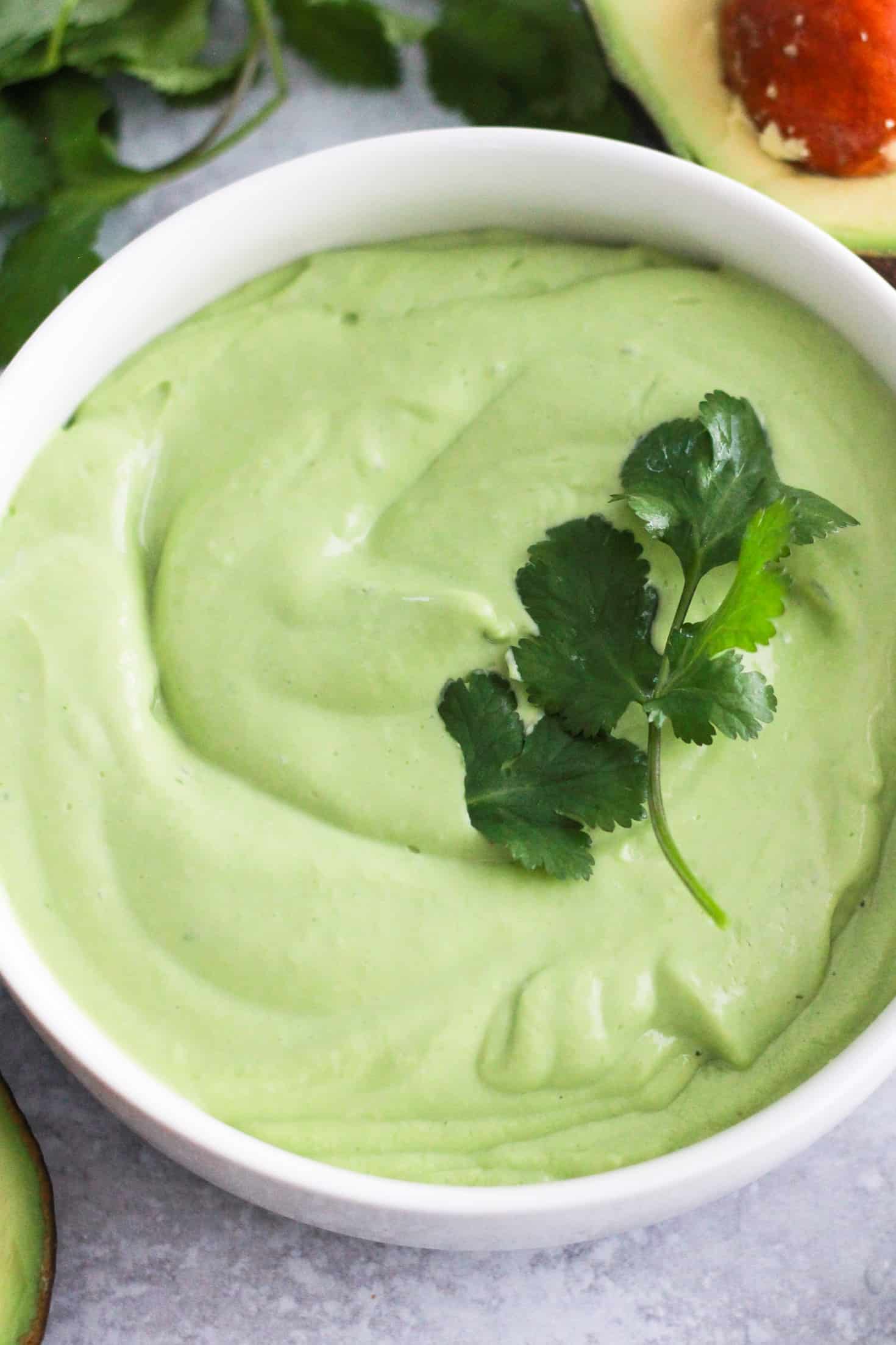 Creamy green avocado crema sauce in white bowl with cilantro.