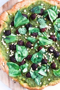 Green vegan pesto pizza on wood board.