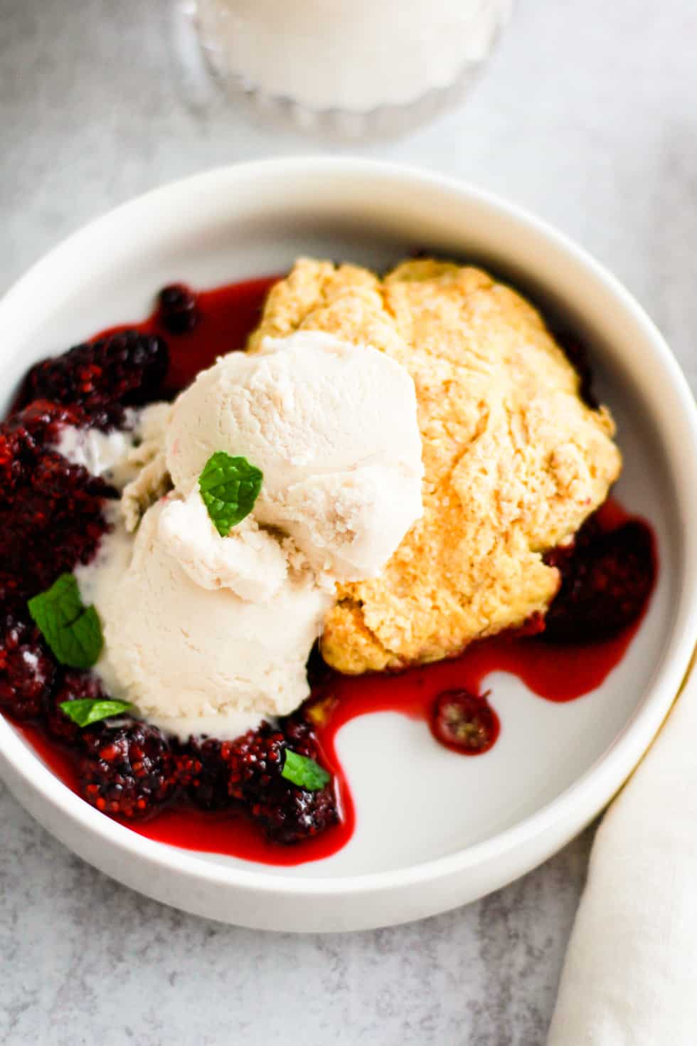 White bowl of vegan blackberry cobbler topped with ice cream and fresh mint.
