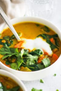 Yellow soup in white bowl with yogurt and cilantro topping.