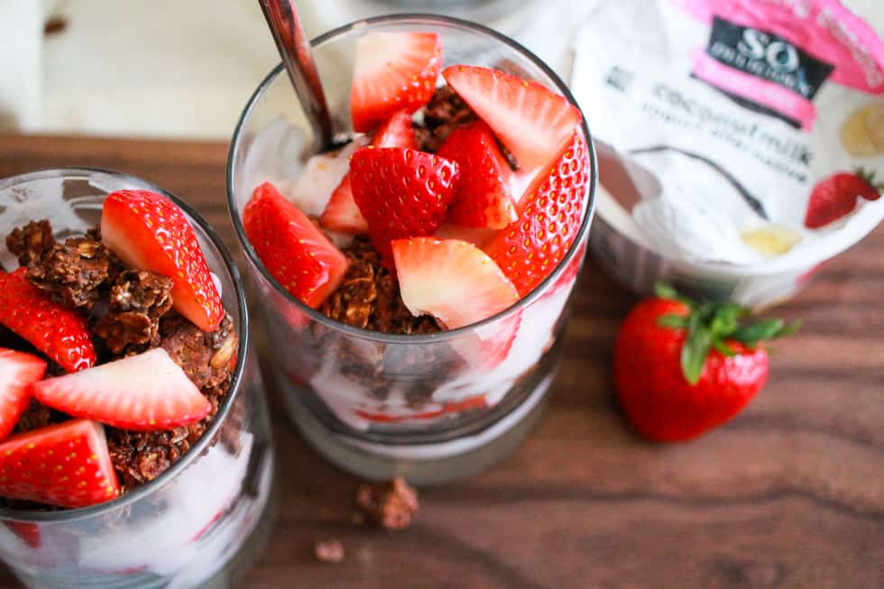 Horizontal image of strawberry yogurt parfaits in glasses with carton of So Delicious yogurt.