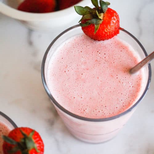 Dairy-free strawberry milkshake with fresh strawberries on white background.