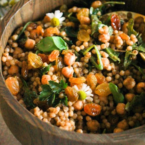 Israeli couscous with chickpeas and golden raisins in a wooden bowl.