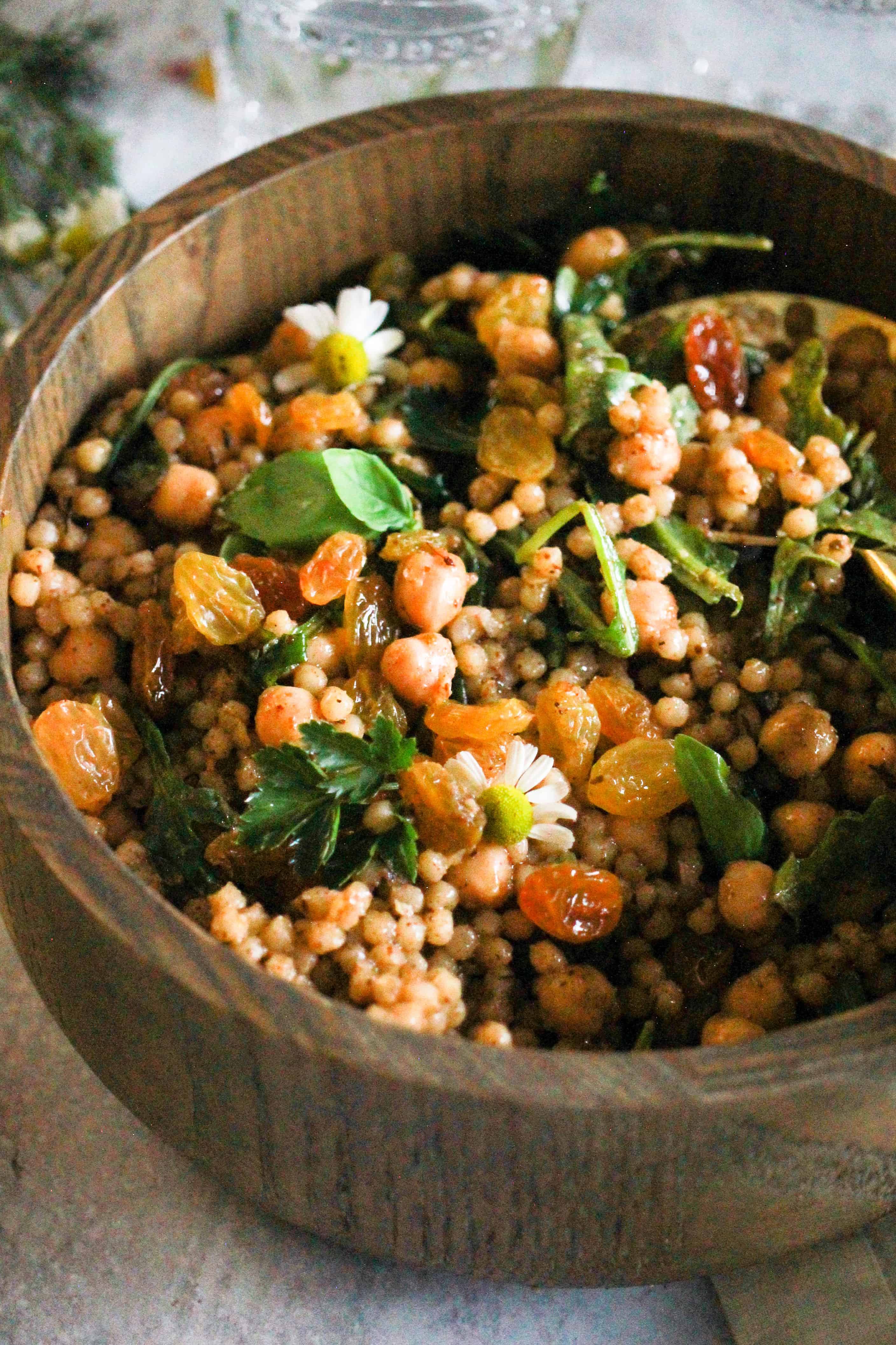 Israeli couscous with chickpeas and golden raisins in a wooden bowl.