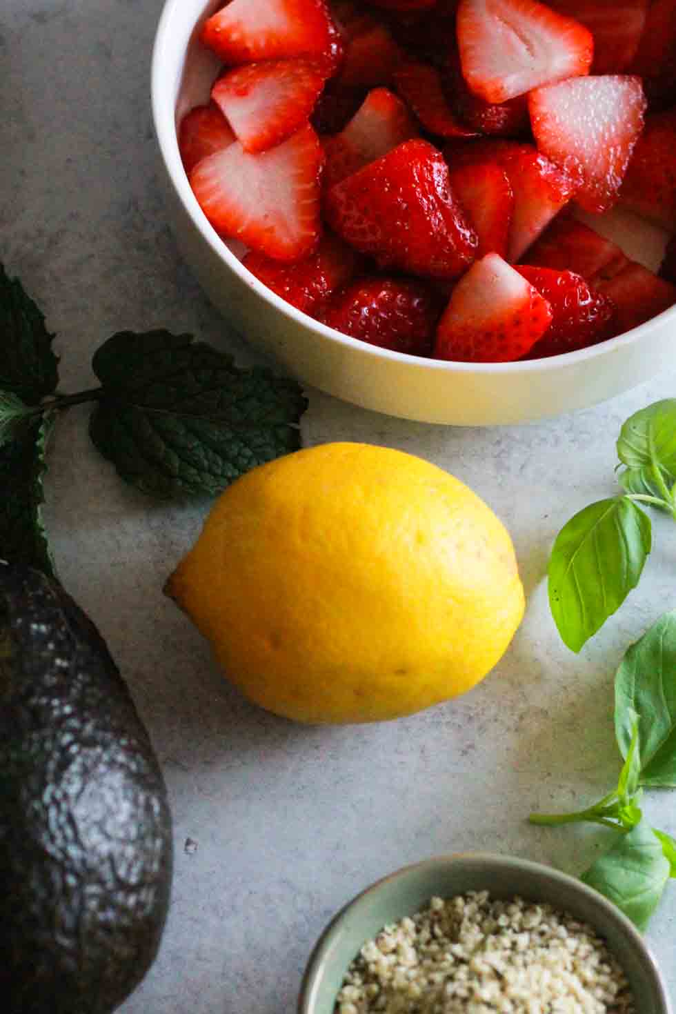 Strawberries, avocado, lemon, basil, and hemp hearts on grey surface.