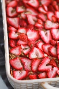 Vegan baked oatmeal topped with strawberries in a white baking dish.
