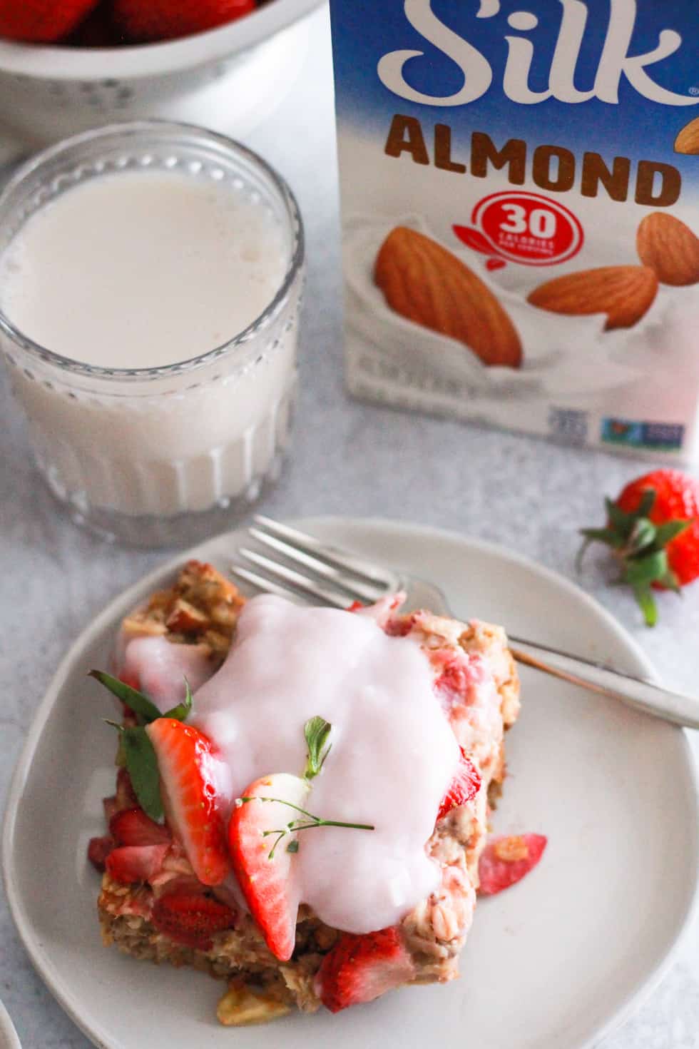 Piece of baked oatmeal with glass of almond milk and carton of Silk.