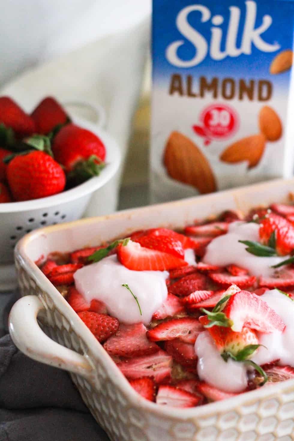 Vegan baked oatmeal in a white dish with fresh strawberries and a carton of Silk almond milk.