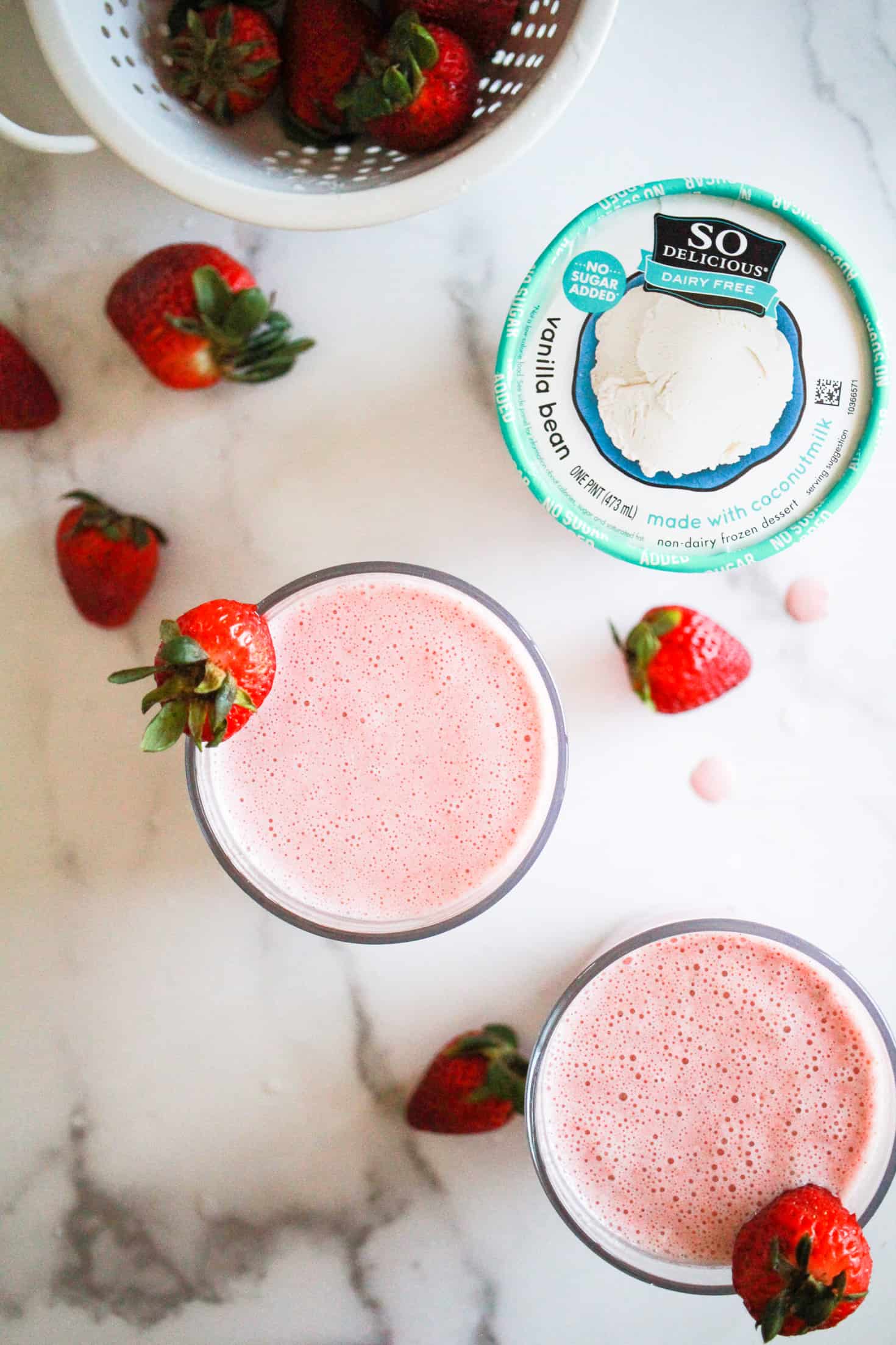 Two strawberry milkshakes with a pint of So Delicious Coconutmilk Ice Cream Alternative and fresh strawberries.