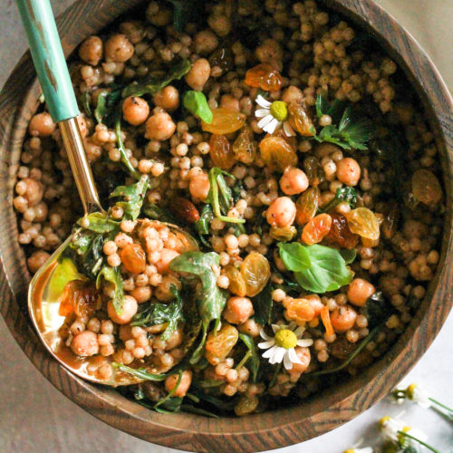 Israeli couscous salad in wooden bowl with blue and gold spoon.