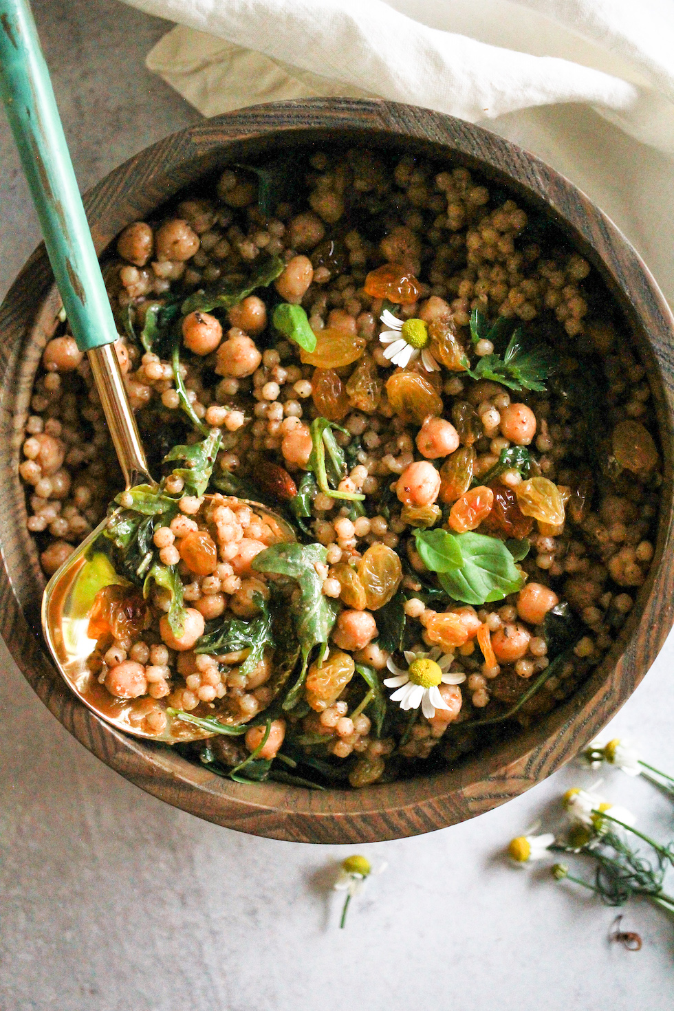 Israeli couscous salad in wooden bowl with blue and gold spoon.