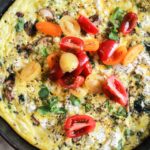 Vertical image of a vegetarian frittata topped with tomatoes in a cast iron skillet.