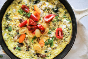 Horizontal image of a vegetarian frittata topped with tomatoes in a skillet.